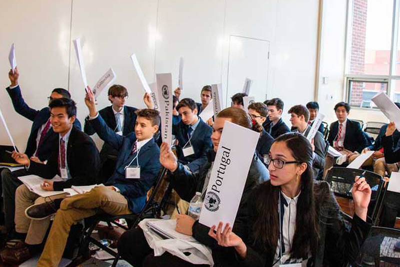 Students in a classroom all raising their hands.