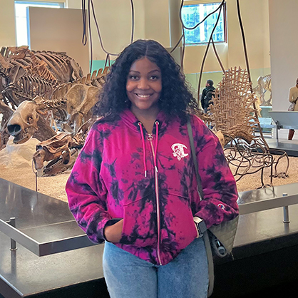 Precious Adesoji ’23 M.S. posing in front of dinosaur bones.