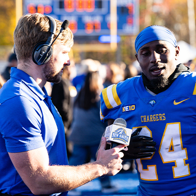 A student broadcaster interviews a football player.