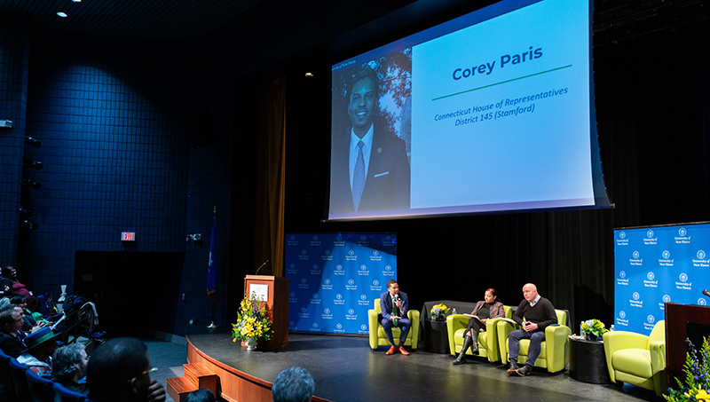 A wide-angle view of the stage where 3 speakers chat sitting in chairs